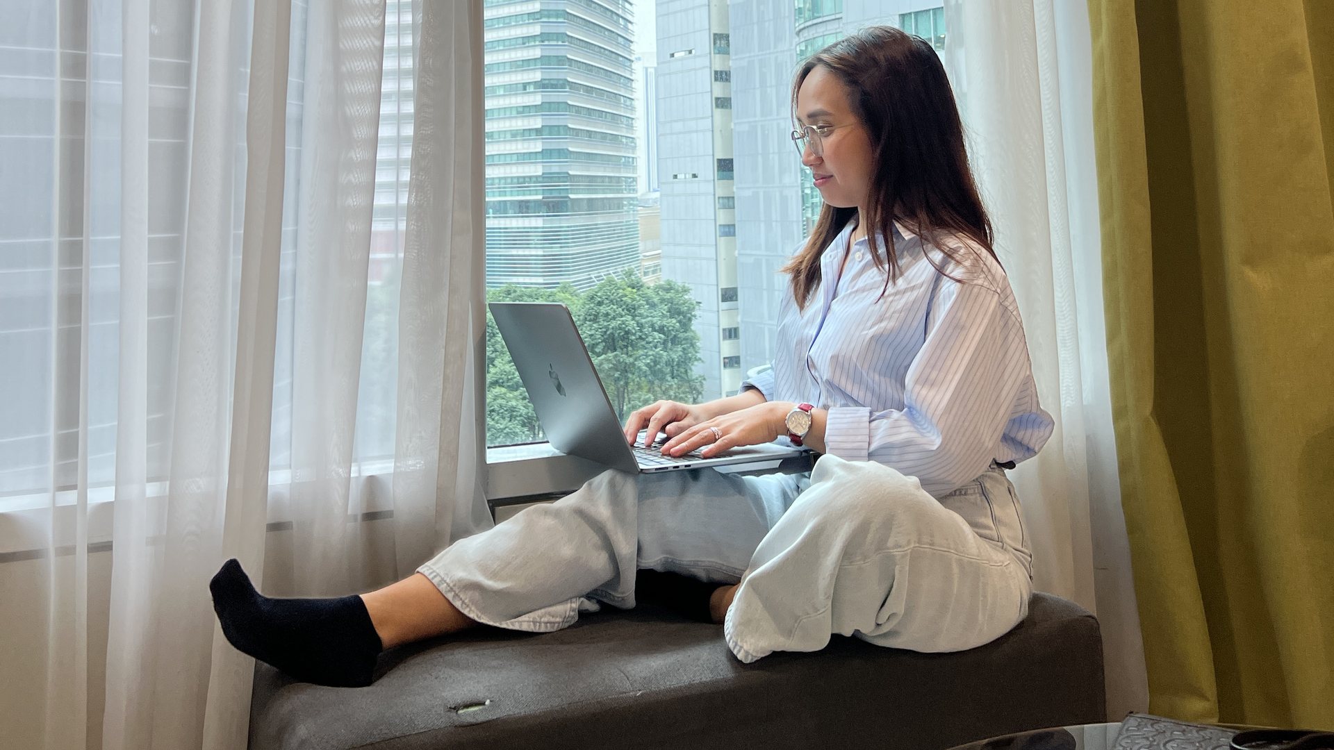 Chelsea Pineda-Astrologio working on a laptop beside a city window.